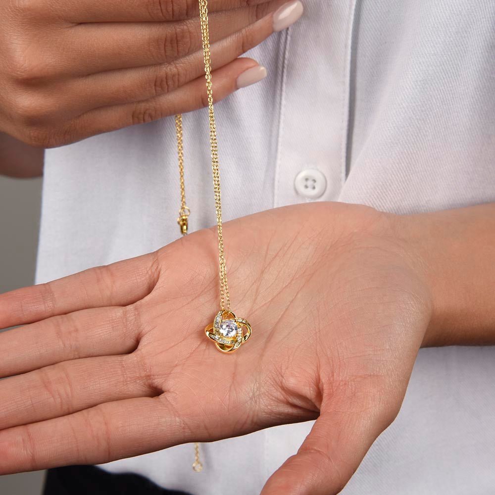 T woman hands holding a 18k yellow gold love knot necklace. 