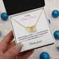  A woman holding A necklace in a gift box with a message to a best friend. The necklace features two interlocking hearts, on gold finish. the background is blue ornaments.