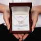  A woman holding A necklace in a luxury gift box with a message to a best friend. The necklace features two interlocking hearts, one silver and one rose gold. 